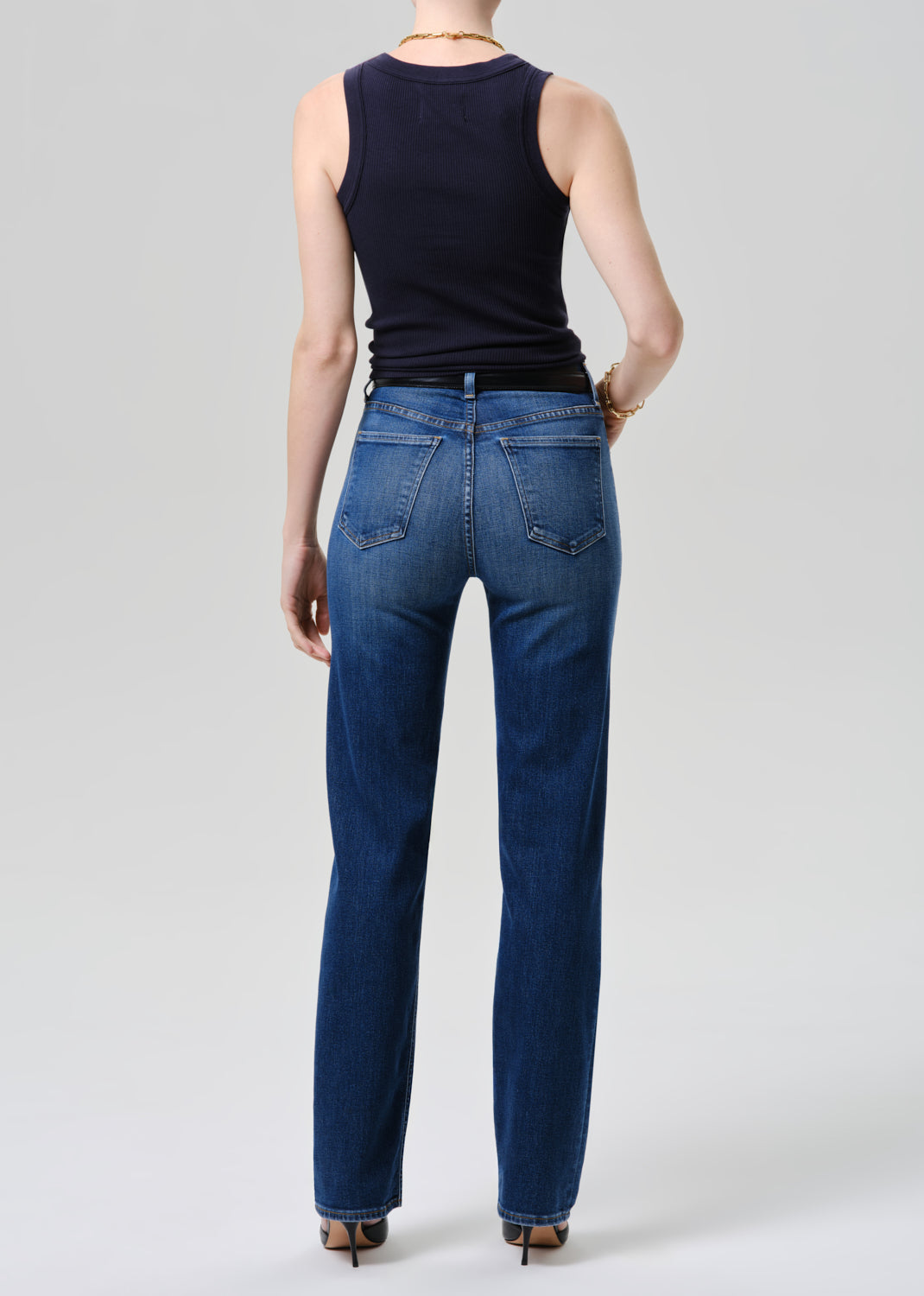 Person wearing blue jeans and a black sleeveless top on a grey background