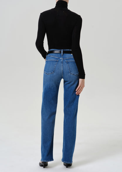 A model shown from the back wearing a black long-sleeve turtleneck top and blue straight-leg jeans, paired with a black belt and black heels, against a light gray studio background.