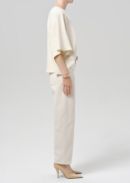 Person wearing beige shirt and off white pants on a grey background