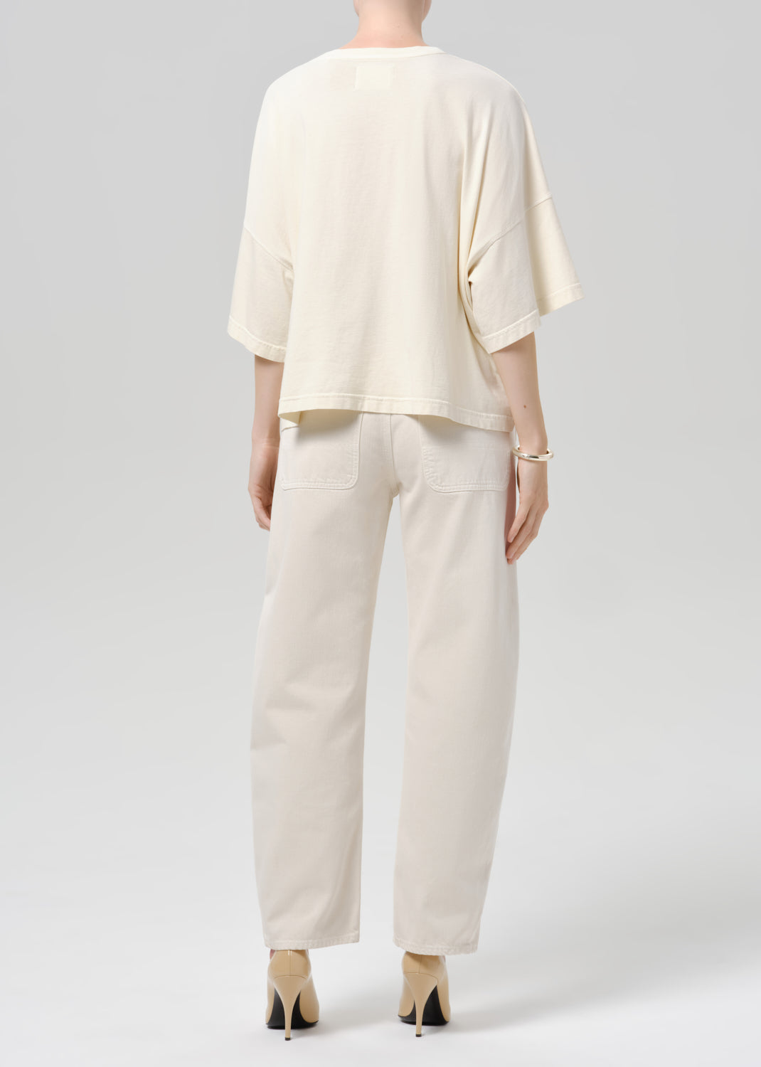 Person wearing beige shirt and off white pants on a grey background