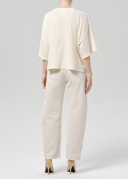 Person wearing beige shirt and off white pants on a grey background