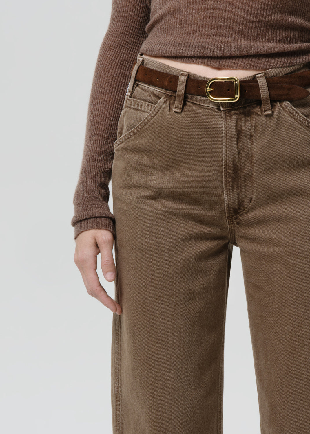 Person wearing brown pants and a matching sweater on a grey background