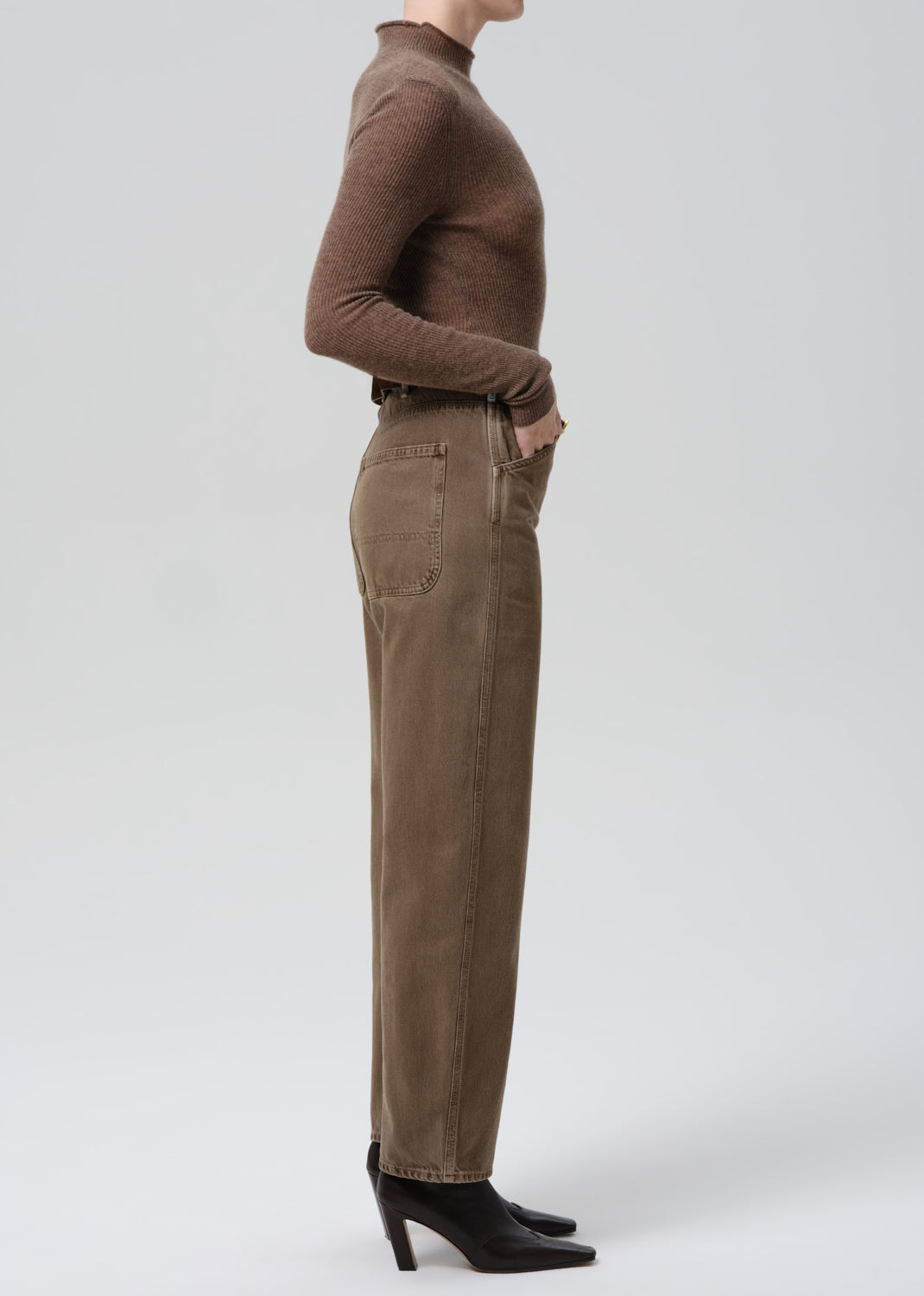 Person wearing a brown turtleneck and beige pants on a grey background
