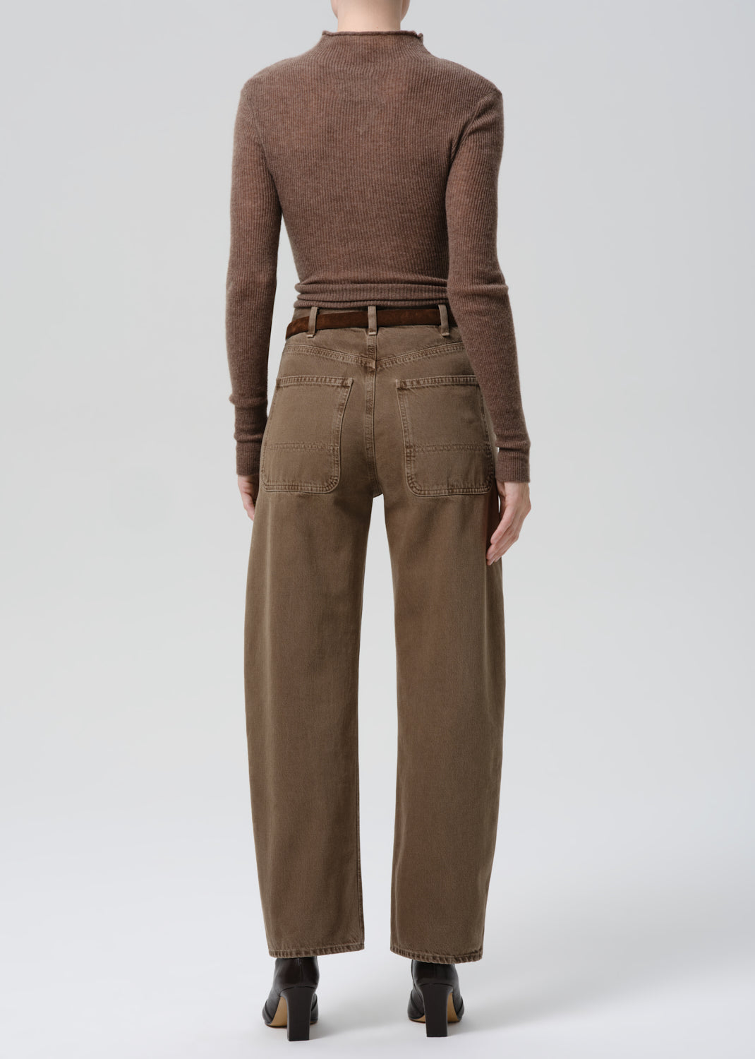Person wearing a brown long-sleeve top and beige pants on a grey background