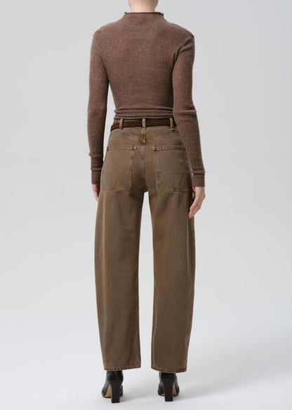 Person wearing a brown long-sleeve top and beige pants on a grey background