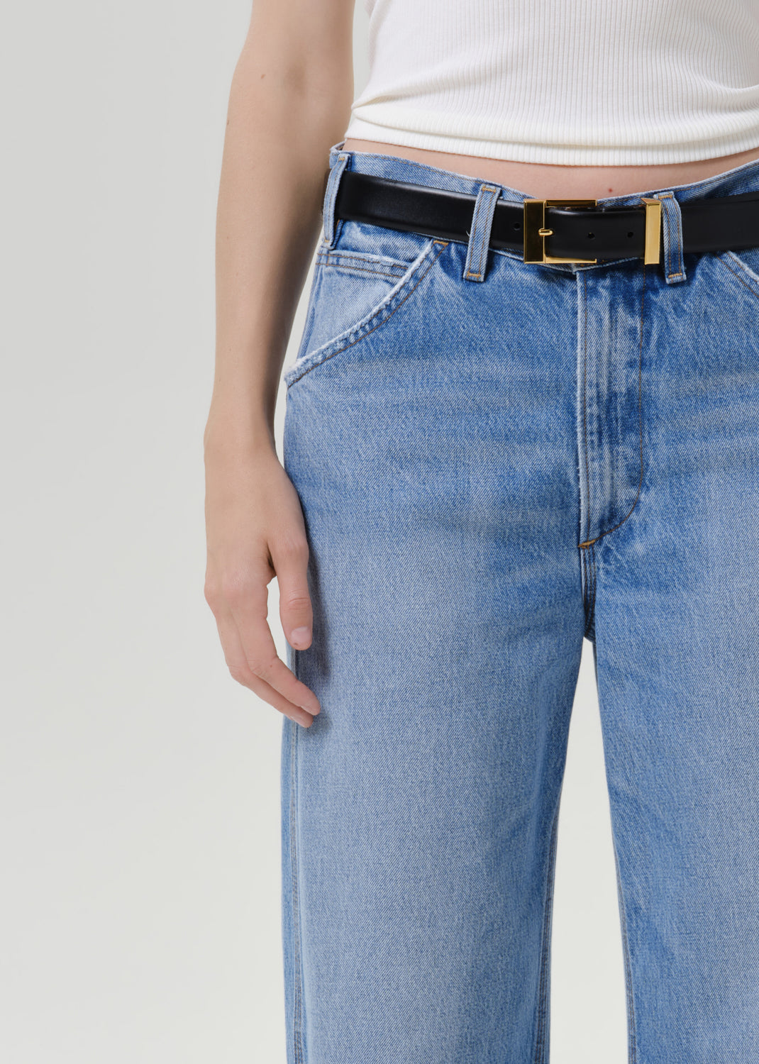 Close up of person wearing blue jeans and a black belt on a grey background