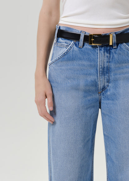Close up of person wearing blue jeans and a black belt on a grey background