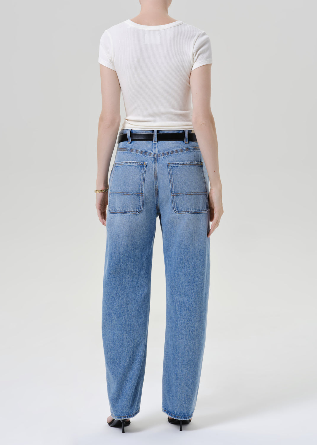 Person wearing a white t-shirt with blue pants on a grey background
