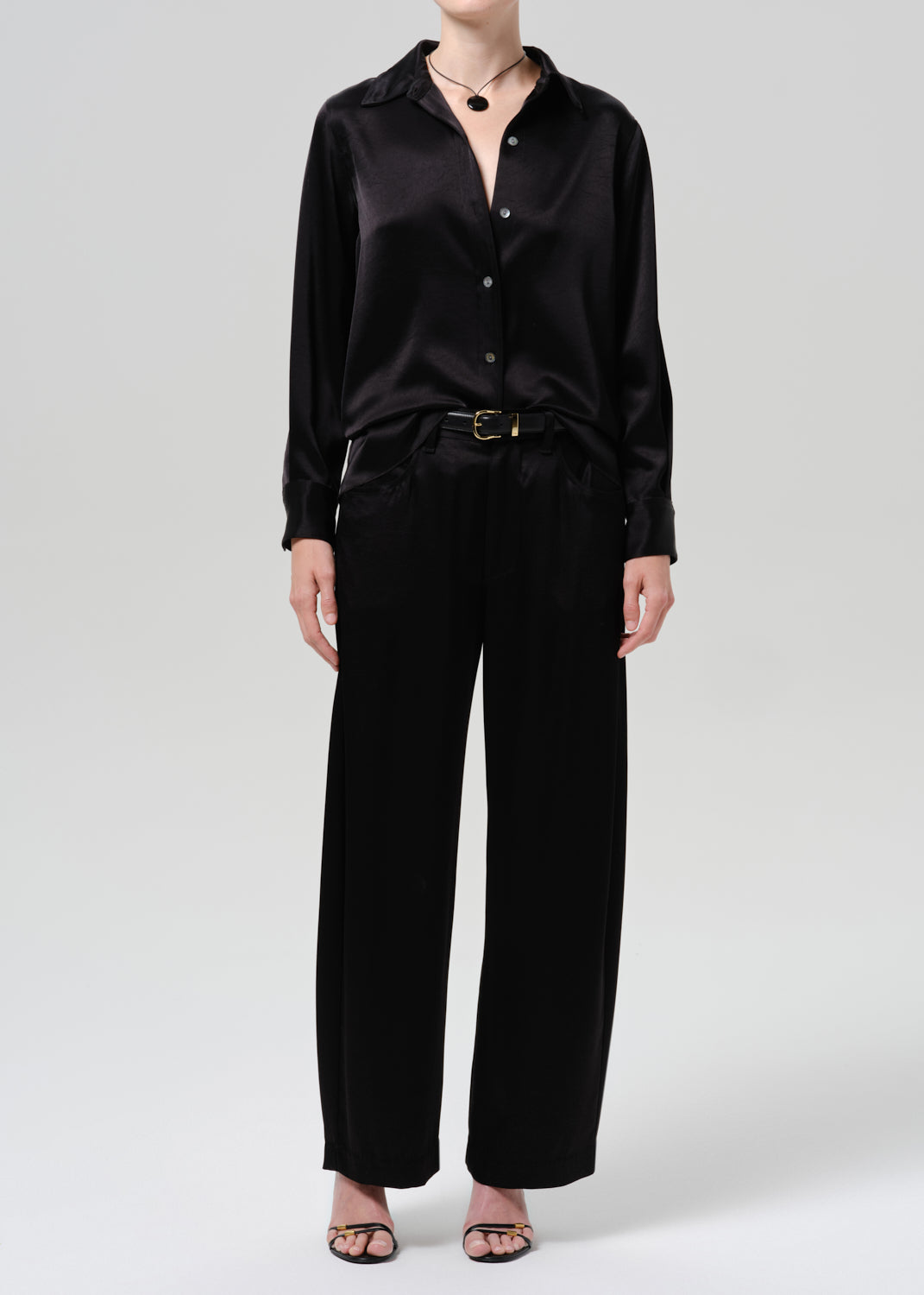 Person wearing a black satin button front blouse with black wide leg trousers on a grey background