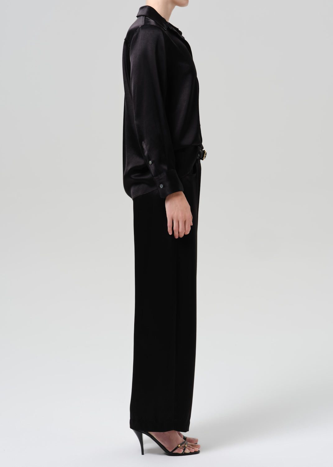Person wearing a black satin button front blouse with black wide leg trousers viewed from the side on a grey background