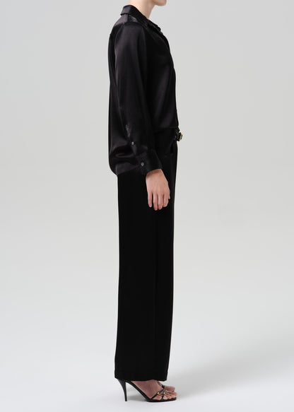 Person wearing a black satin button front blouse with black wide leg trousers viewed from the side on a grey background