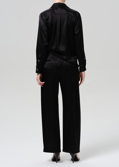 Person wearing a black satin button front blouse with black wide leg trousers viewed from the back on a grey background