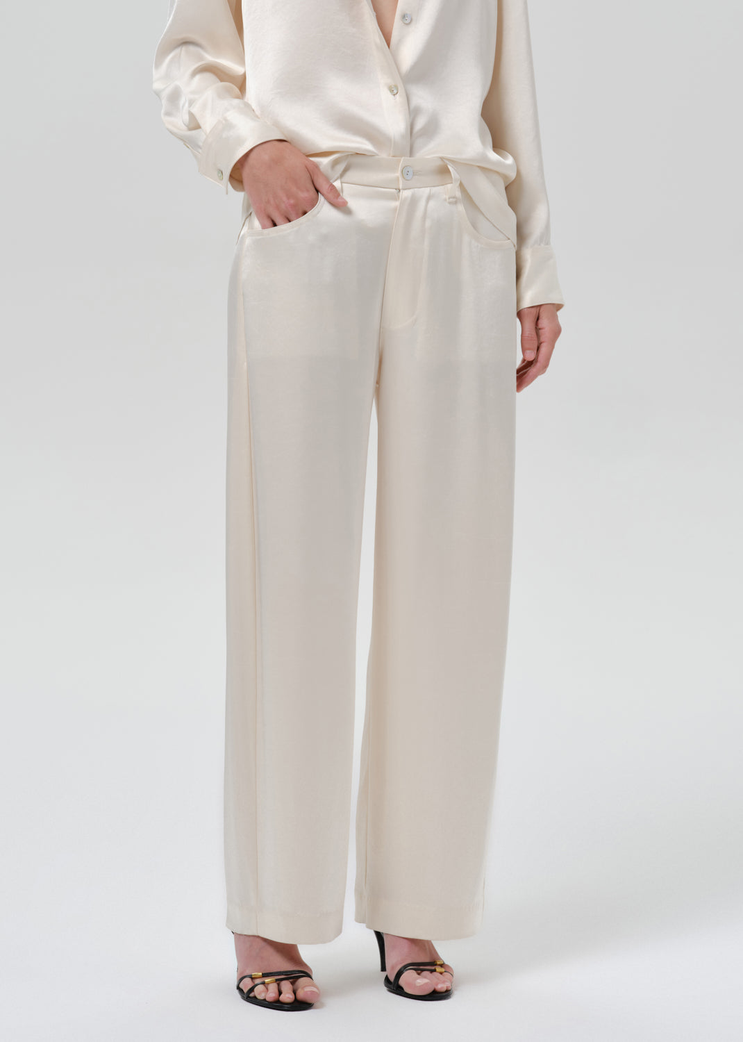 Person wearing an ivory satin button front blouse with ivory wide leg trousers on a grey background