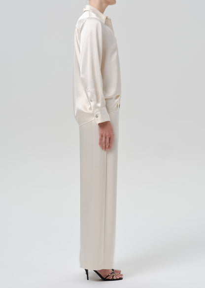 Person wearing an ivory satin button front blouse with ivory wide leg trousers viewed from the side on a grey background