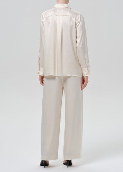 Person wearing an ivory satin button front blouse with ivory wide leg trousers viewed from the back on a grey background