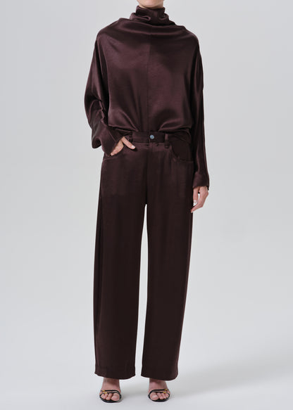 A model wearing a dark brown satin long-sleeve top with a cowl neck and matching wide-leg trousers, styled with black strappy heels against a grey background.