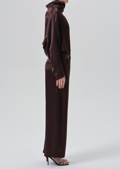 A model shown from the side wearing a dark brown satin turtleneck top and matching wide-leg trousers with a tie belt at the waist, paired with black high-heeled sandals, against a grey background.