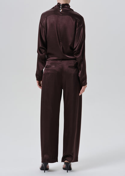 A model shown from the back wearing a matching dark plum satin tracksuit with a high-neck top and wide-leg trousers, paired with black pointed-toe heels, against a grey background.