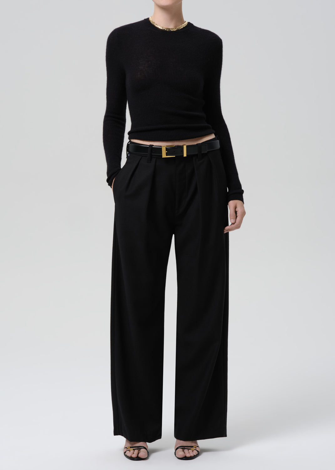 Person wearing a black fitted long sleeve sweater with black wide leg trousers on a grey background