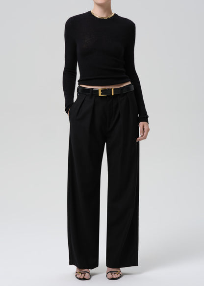 Person wearing a black fitted long sleeve sweater with black wide leg trousers on a grey background