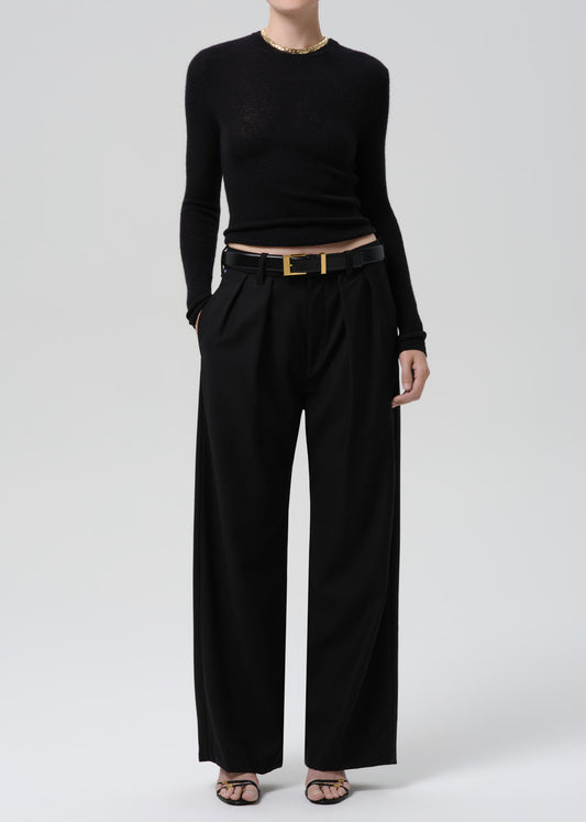 Person wearing a black fitted long sleeve sweater with black wide leg trousers on a grey background