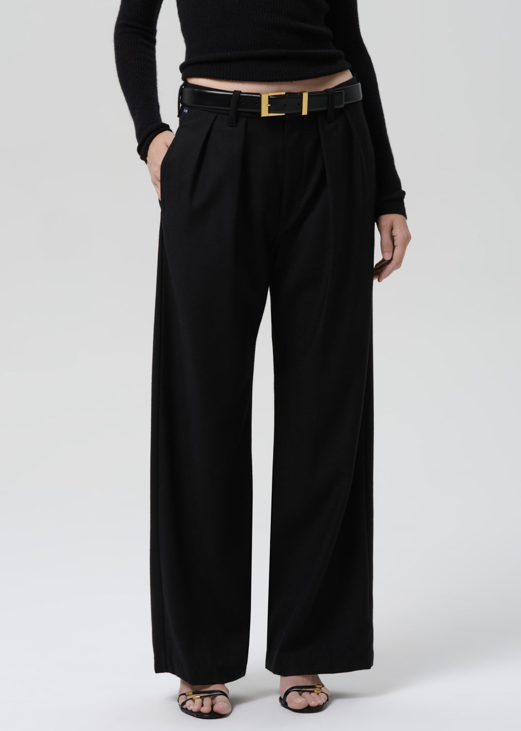 Person wearing a black fitted long sleeve sweater with black wide leg trousers on a grey background