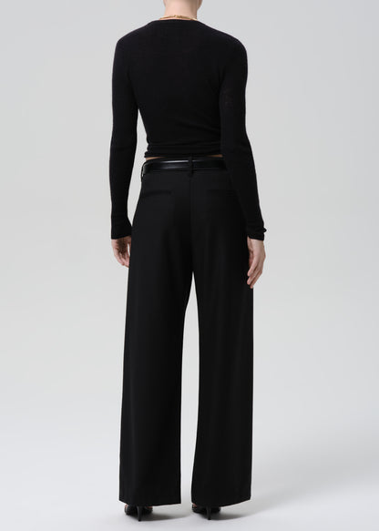 Person wearing a black fitted long sleeve sweater with black wide leg trousers viewed from the back on a grey background