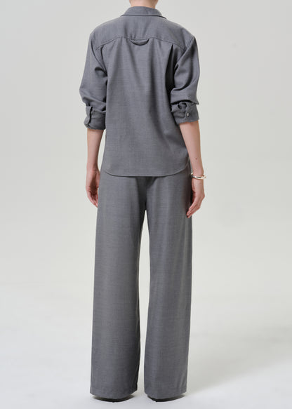 A model shown from the back wearing a gray two-piece set consisting of a long-sleeve button-down shirt and matching wide-leg trousers, photographed against a neutral light gray studio background.