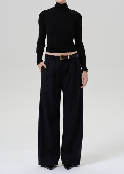 Person wearing a black fitted turtleneck with dark navy wide leg trousers on a grey background