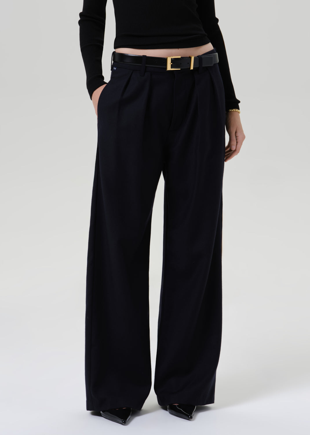 Person wearing a black fitted turtleneck with dark navy wide leg trousers on a grey background