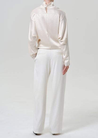Woman wearing white wide leg pants with an ivory satin draped neck top on a grey background.