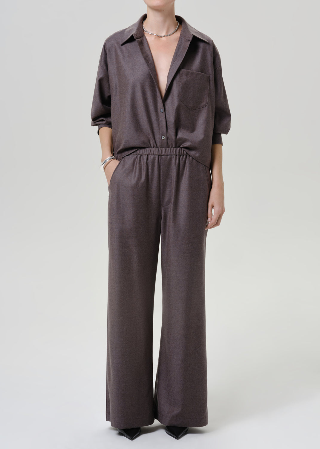Woman wearing dark brown wide leg pants with a matching dark brown short sleeve top on a grey background.
