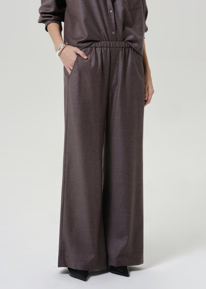 Woman wearing dark brown wide leg pants with a matching dark brown short sleeve top on a grey background.