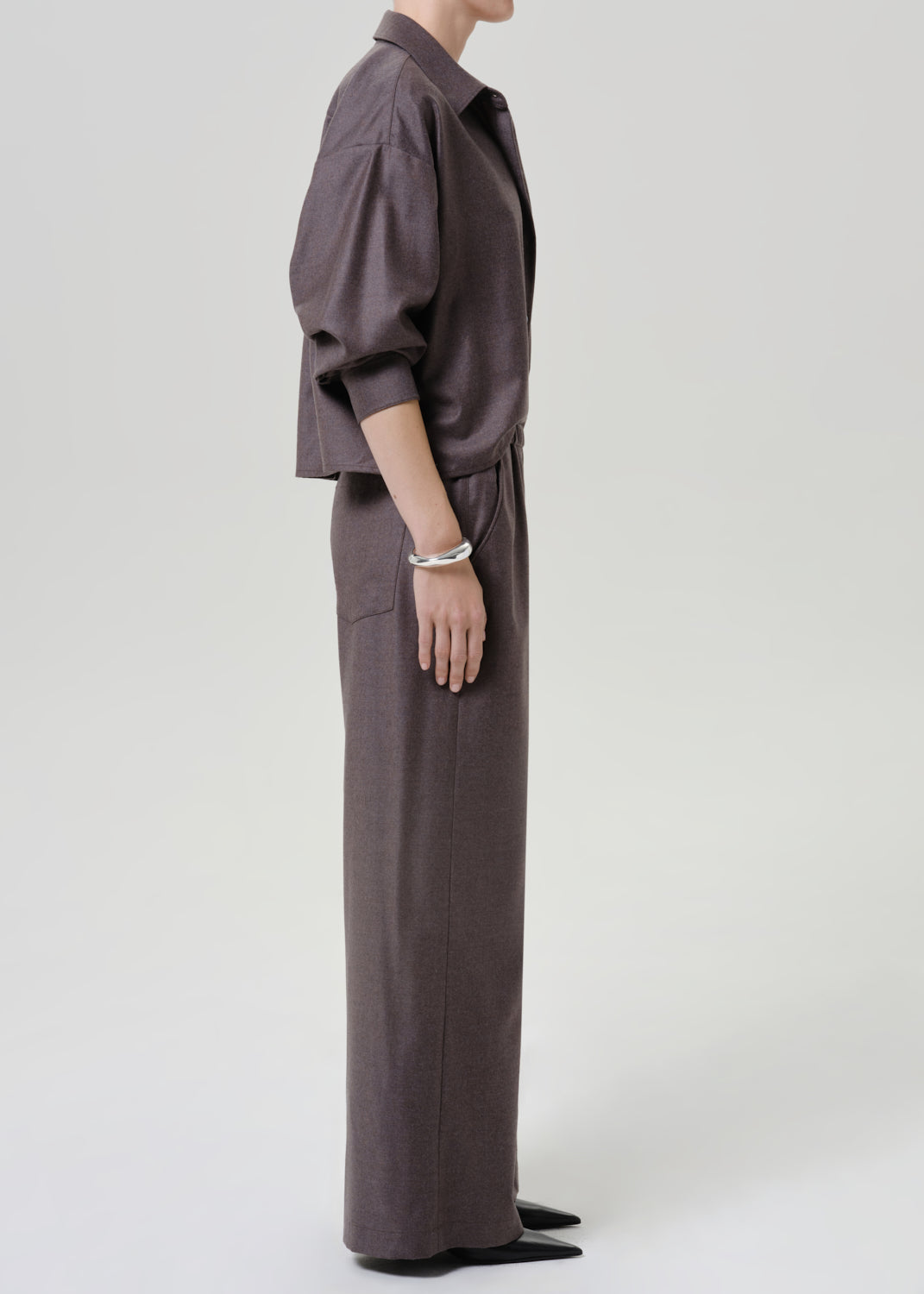 Woman wearing dark brown wide leg pants with a matching dark brown short sleeve top viewed from the side on a grey background.