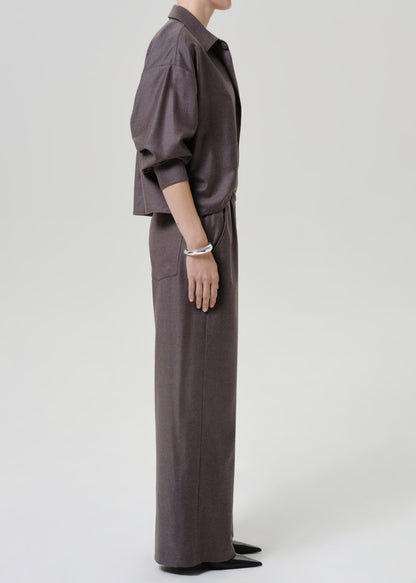 Woman wearing dark brown wide leg pants with a matching dark brown short sleeve top viewed from the side on a grey background.