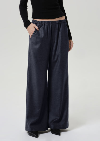 Woman wearing dark grey wide leg pants with a black long sleeve top on a grey background.
