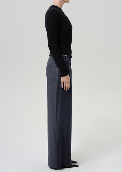 Woman wearing dark grey wide leg pants with a black long sleeve top viewed from the side on a grey background.