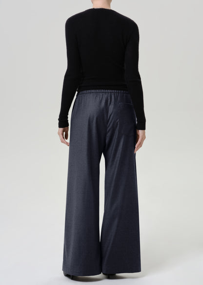 Woman wearing dark grey wide leg pants with a black long sleeve top viewed from the back on a grey background.