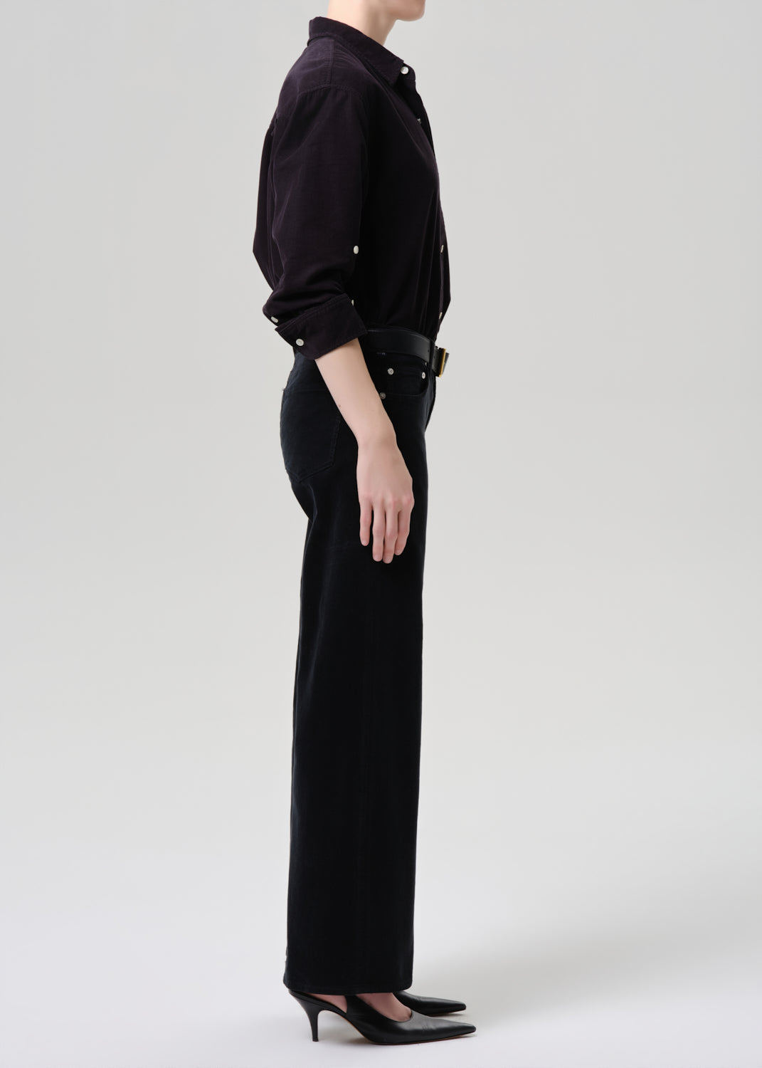 Person wearing a black outfit with a high collar and wide-leg pants on a grey background
