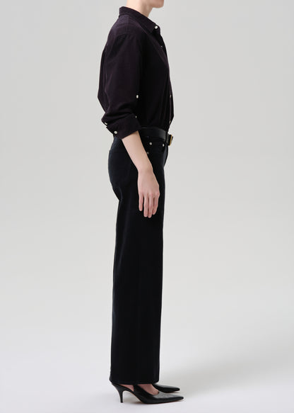 Person wearing a black outfit with a high collar and wide-leg pants on a grey background