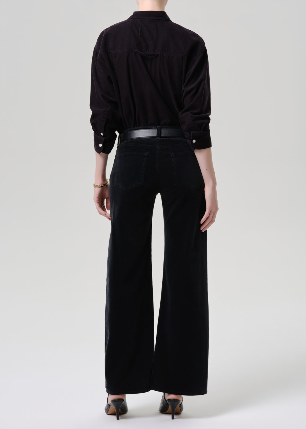 Person wearing a black outfit with wide-leg pants on a grey background