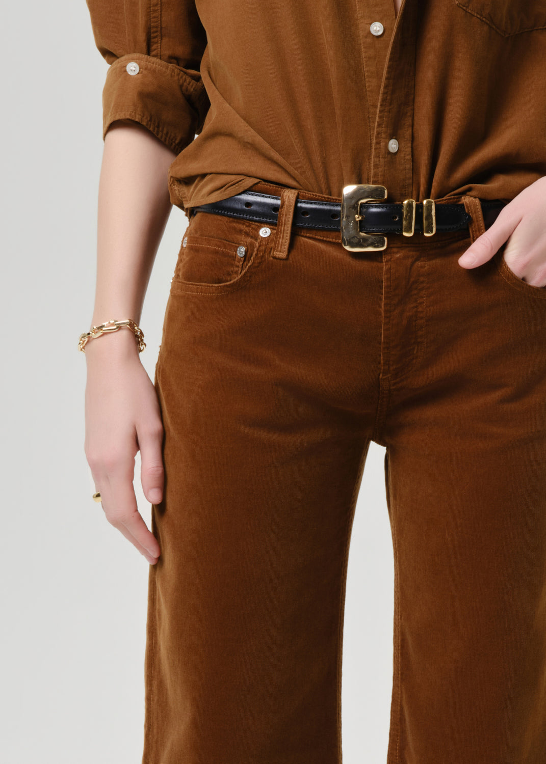 Person wearing a brown jumpsuit with a belt on a grey background