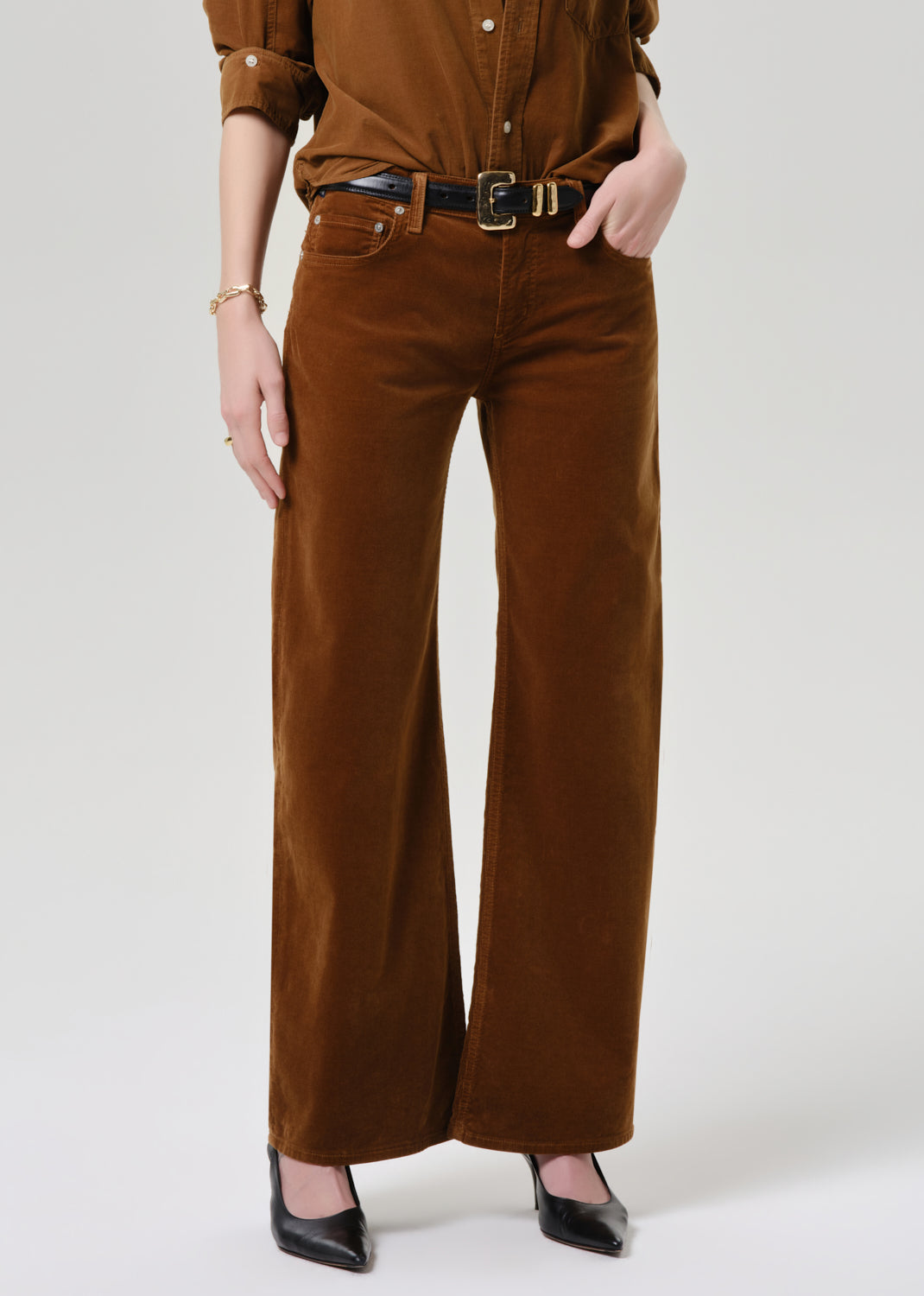 Person wearing a brown shirt and wide-leg pants on a grey background