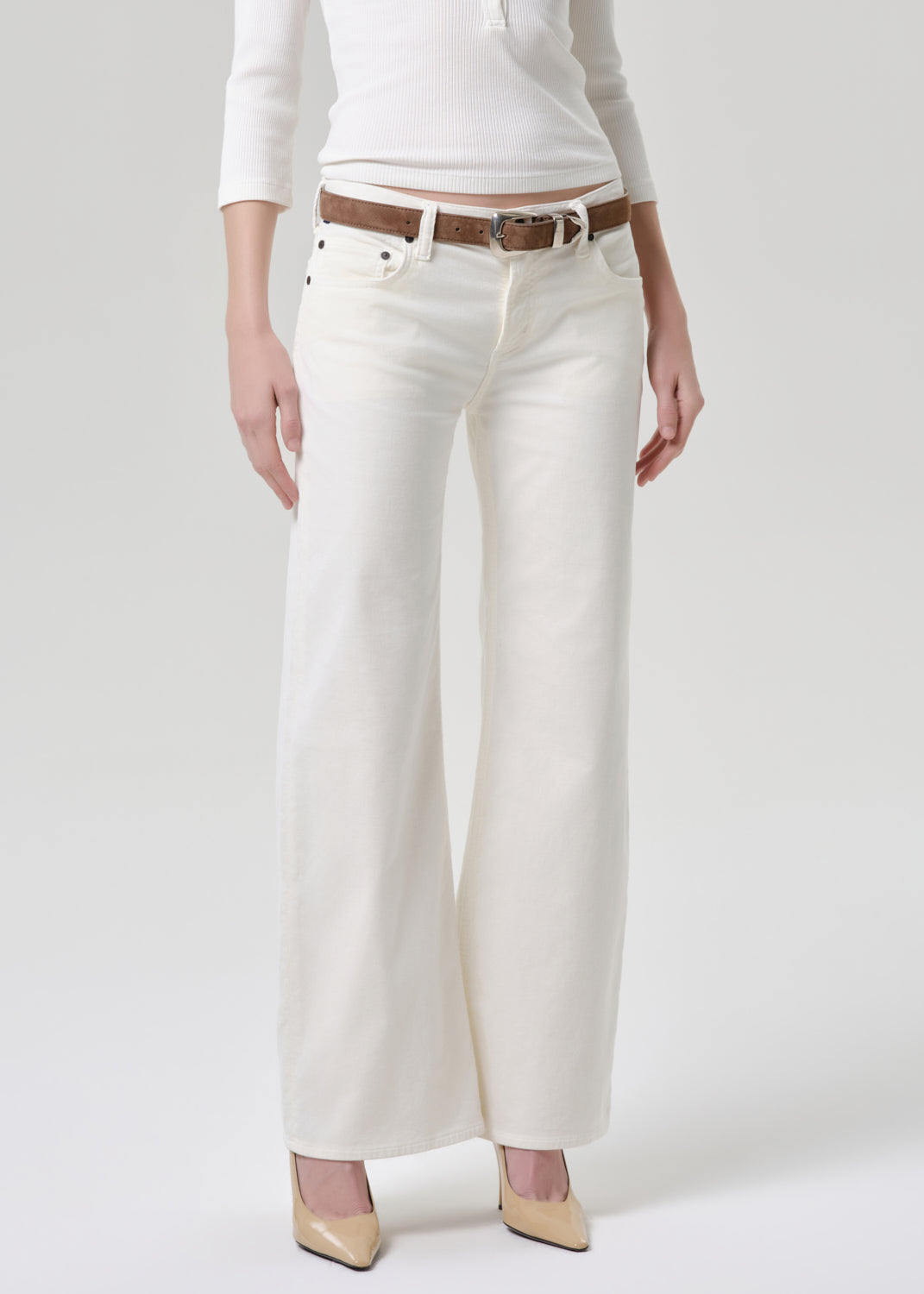 Person wearing white pants with a brown belt on a grey background