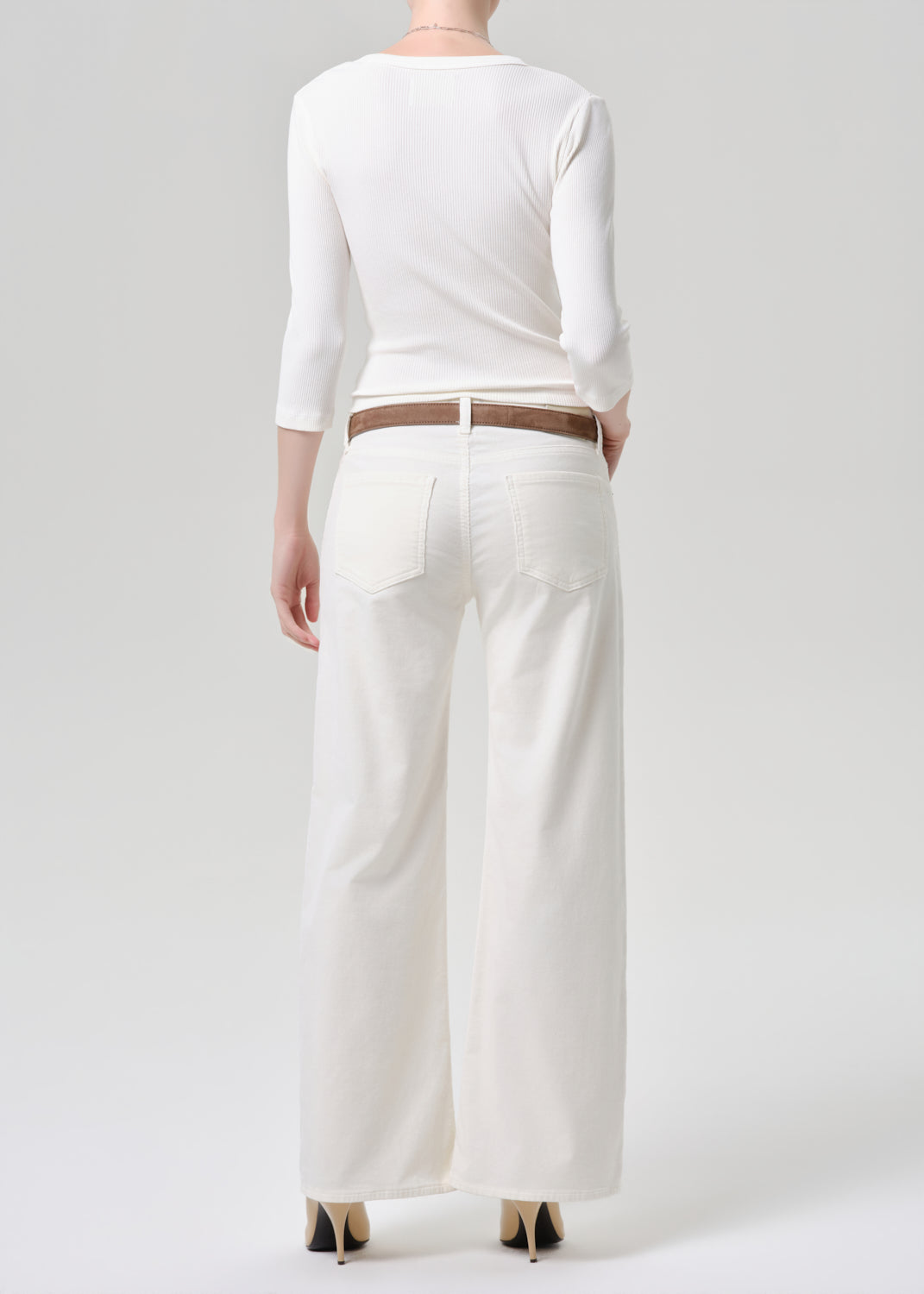 Person wearing a white outfit with wide-leg pants on a grey background