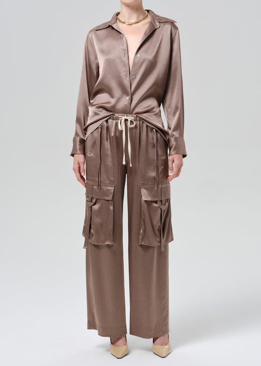 Person wearing silk brown shirt and pants on a grey background