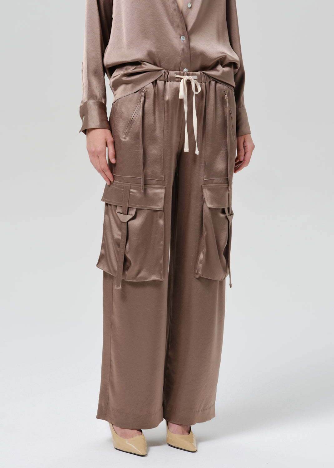 Person wearing silk brown pants on a grey background