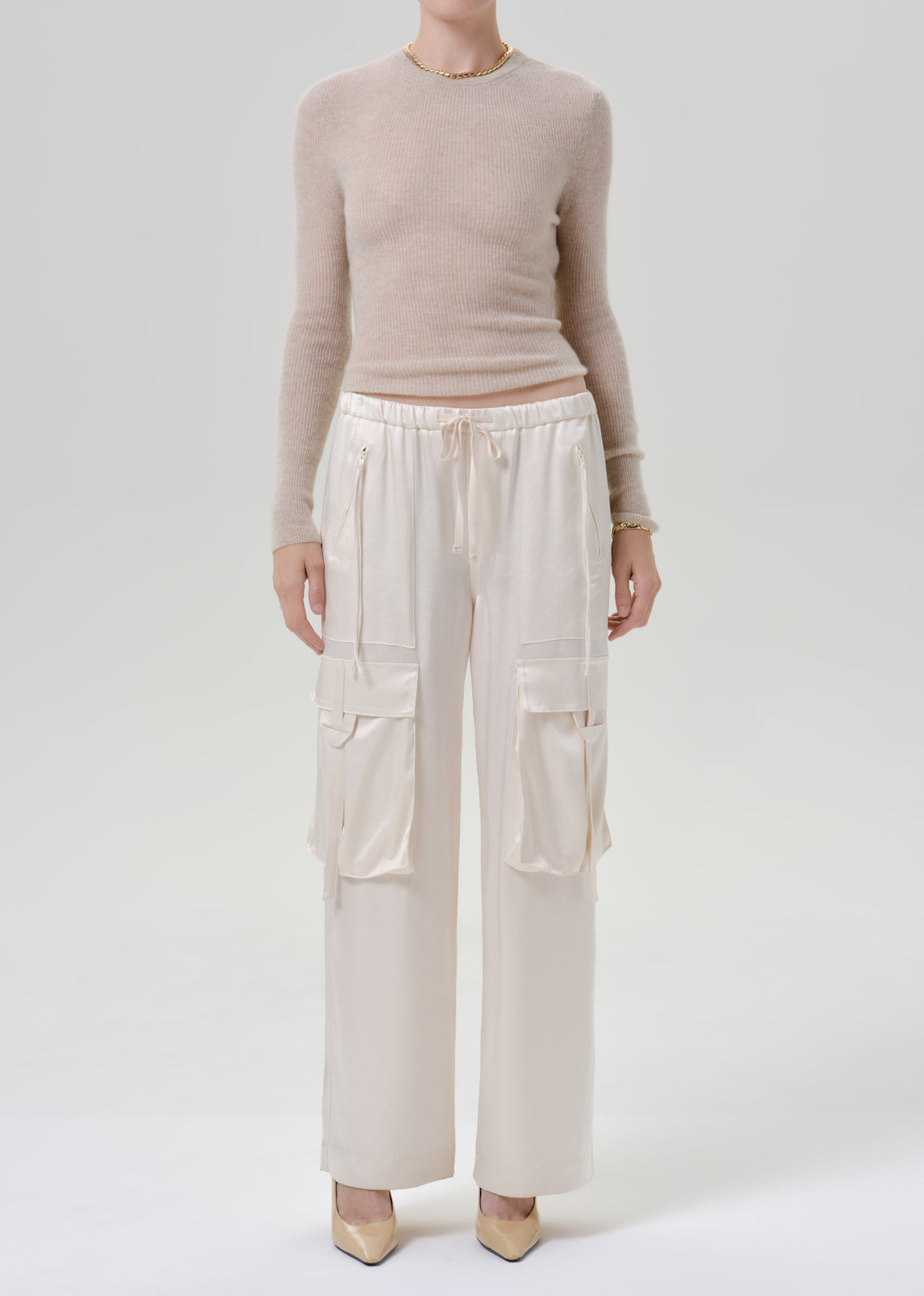 Person wearing beige long sleeve with white pants on a grey background