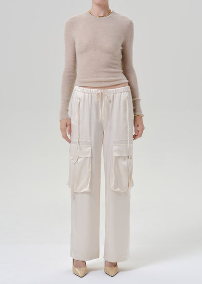 Person wearing beige long sleeve with white pants on a grey background