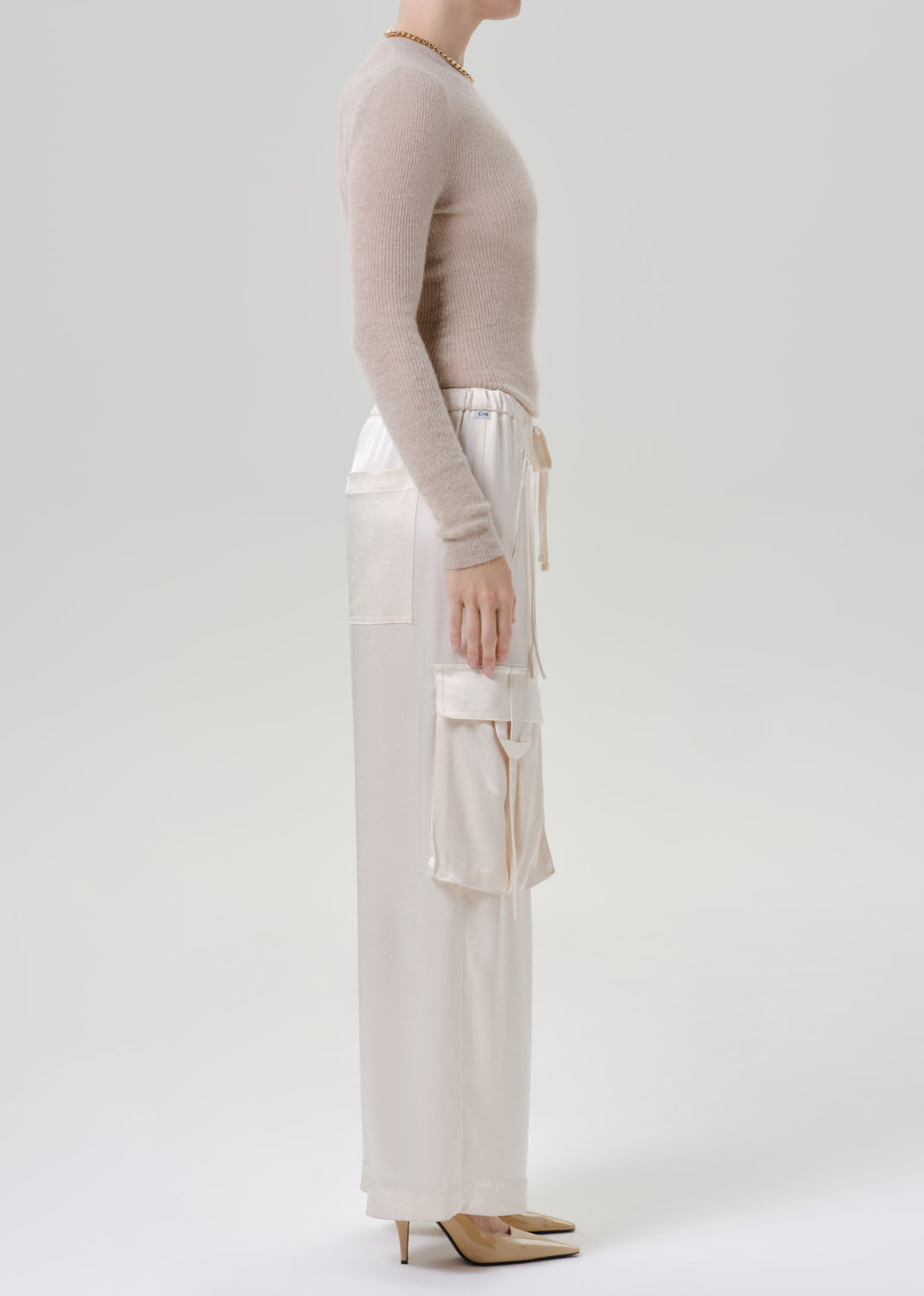 Person wearing beige long sleeve with white pants on a grey background